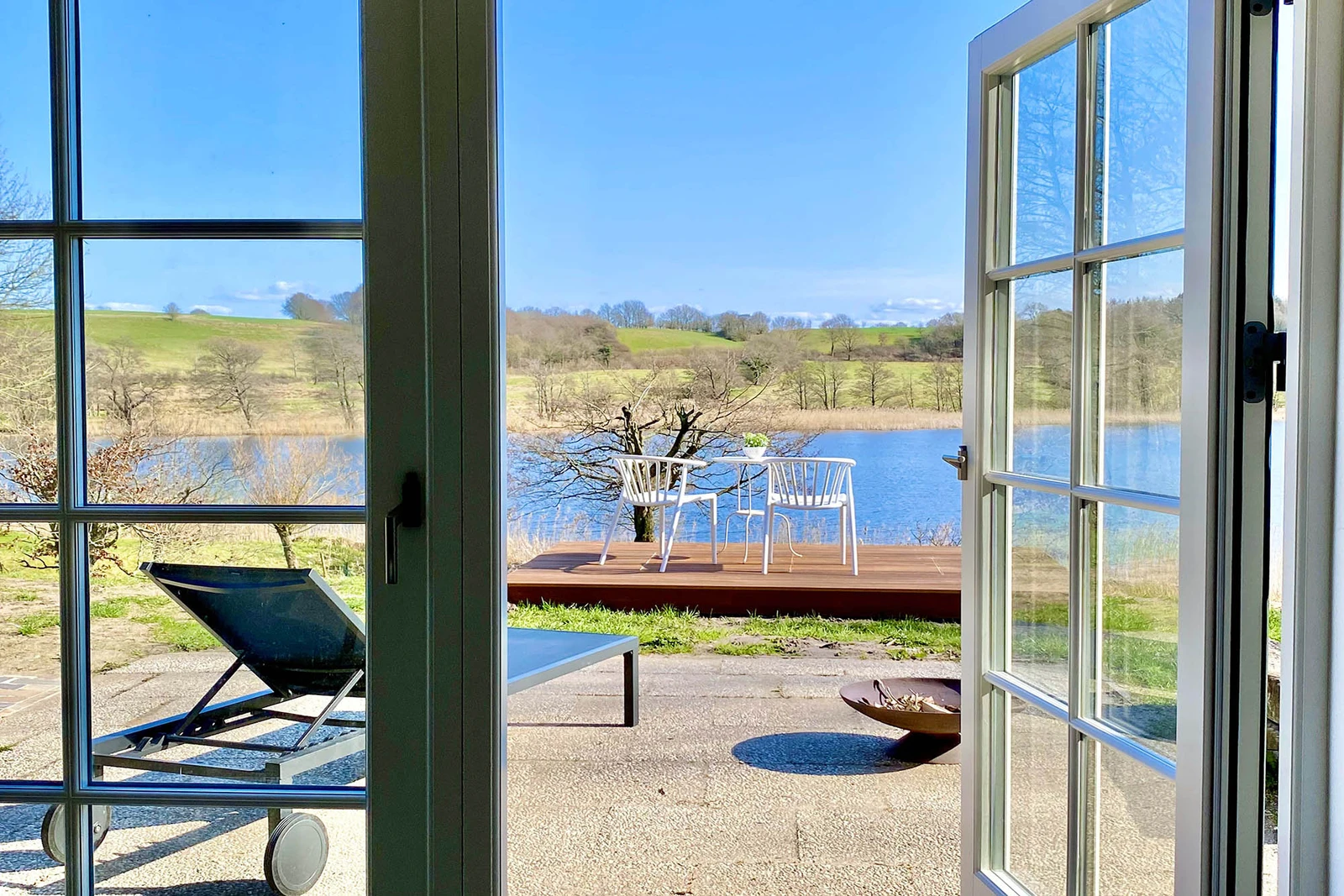 Ausblick durch geöffnete Terrassentür auf Terrasse und Niehuuser See